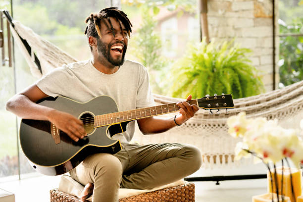 Smiling young male musician playing an acoustic guitar outside on a patio in summer